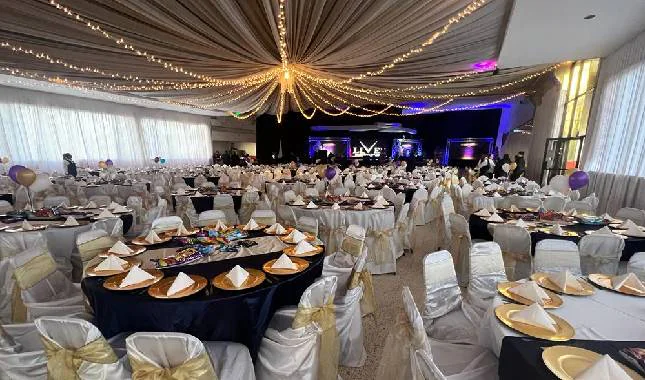 Mesas redondas con mantel negro, vajilla dorada y sillas vestidas en el salón