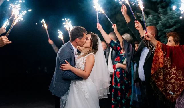 Novios besándose entre invitados que sostienen bengalas encendidas