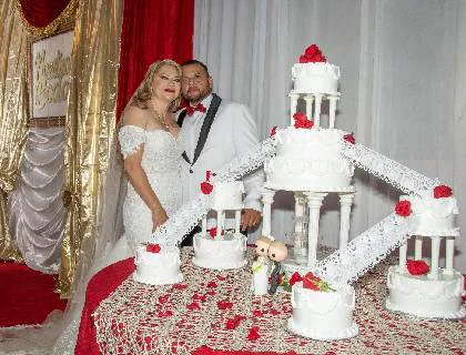 Novios cortando el pastel de bodas frente al cortinaje del salón