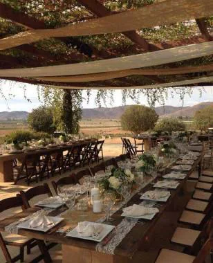 Mesa larga montada bajo vigas de madera para una boda en el Valle de Guadalupe
