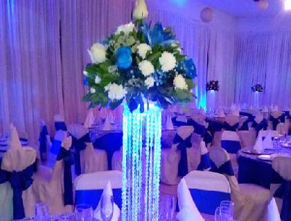 Centro de mesa con flores blancas y azules sobre columna de cristal iluminada