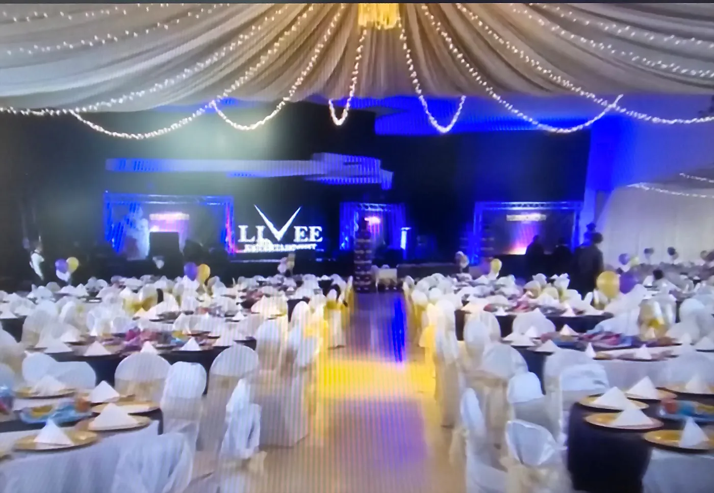 Salón montado para una graduación, con escenario iluminado al fondo y pista al centro
