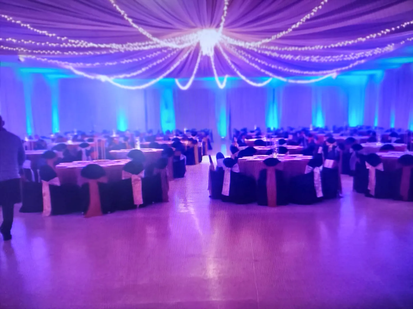 Vista amplia del salón montado con mesas redondas e iluminación morada y cian