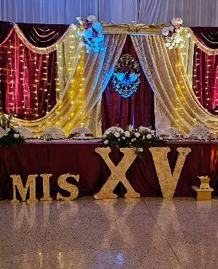 Letras iluminadas «MIS XV» sobre cortinaje rojo y dorado en el salón